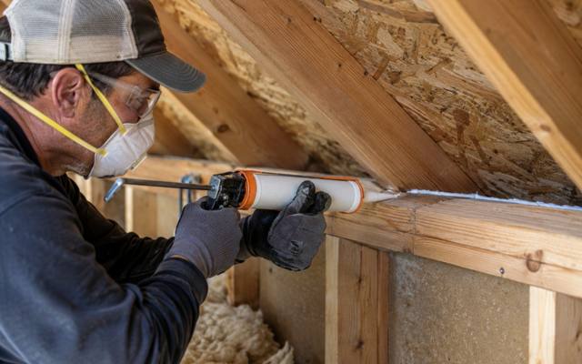 Caulking gun sealing the gap along a top plate in an attic