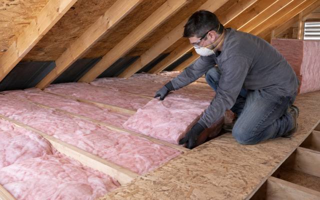Installer laying pink batt insulation between sloped attic rafters