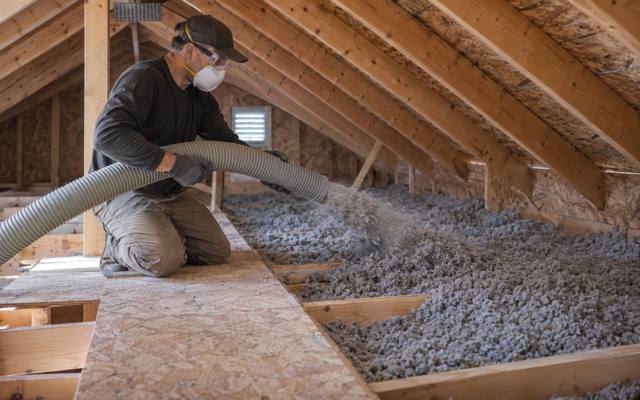 Installer topping up an attic with blown cellulose insulation between the trusses