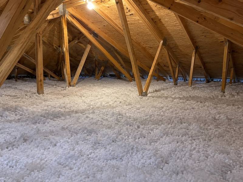 White blown-in fiberglass insulation spread across a wide attic under the roof trusses